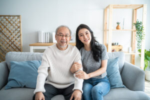 Portrait of Asian lovely family, daughter hugging and sit with father. Attractive woman granddaughter visit senior elder mature man in house enjoy spend leisure time together smile and look at camera.