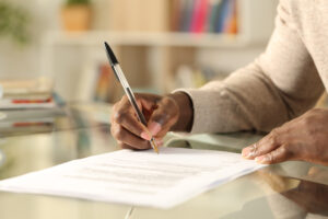 Close up of black man hands signing document on a desk at home